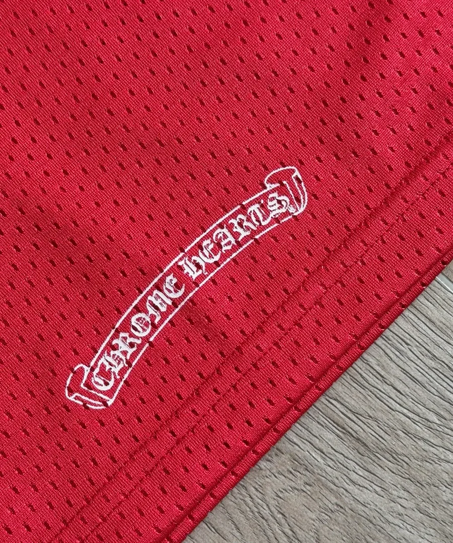 Деталь вышивки Chrome Hearts на нижней кромке красной футболки-джерси