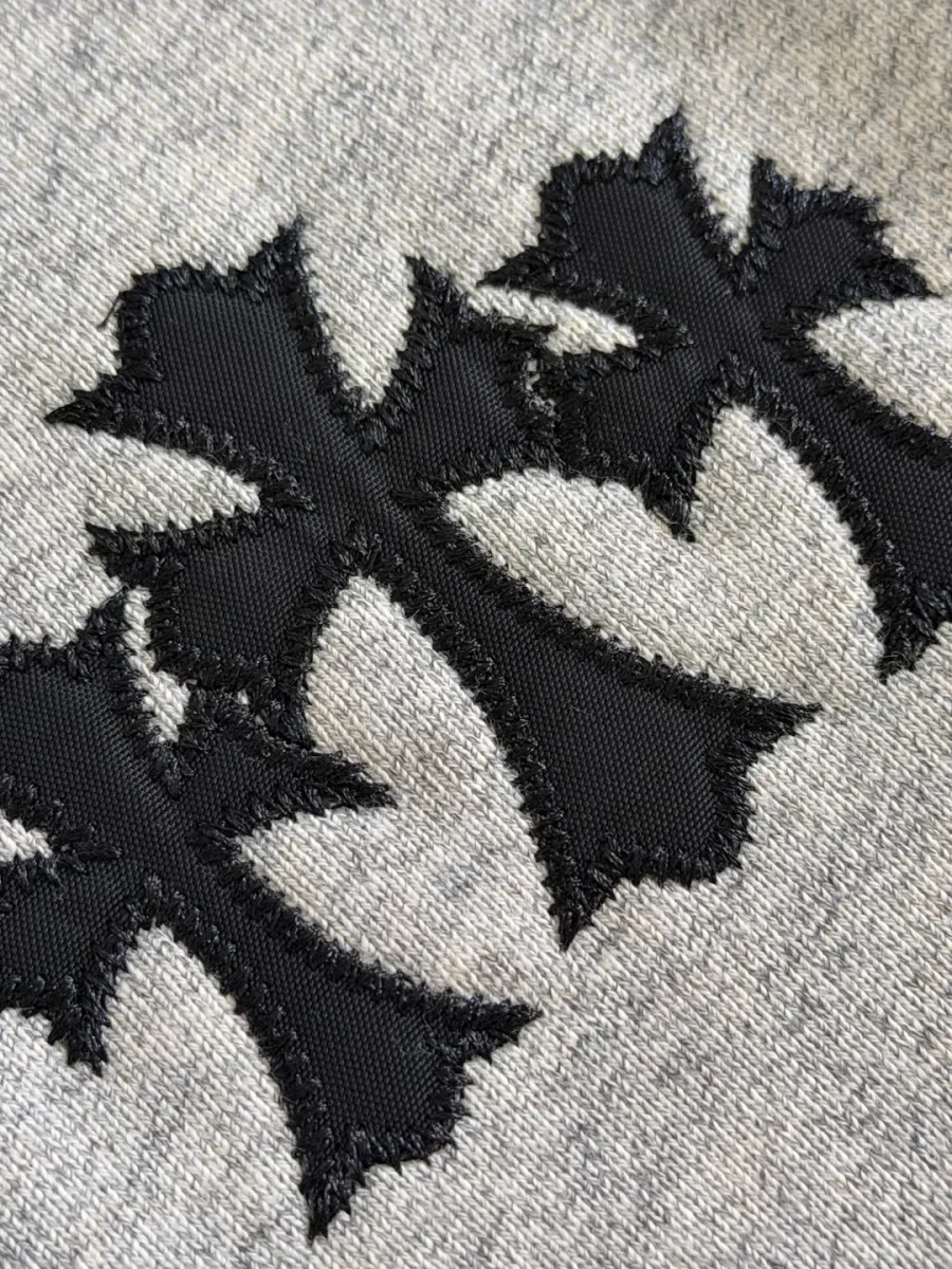 Деталь аппликации в виде трех черных крестов на груди худи Chrome Hearts