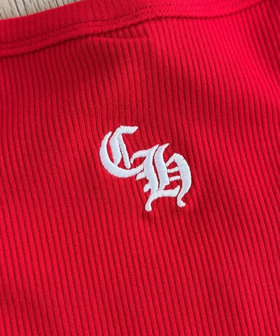 Деталь вышивки с логотипом CH белого цвета на красном трикотаже