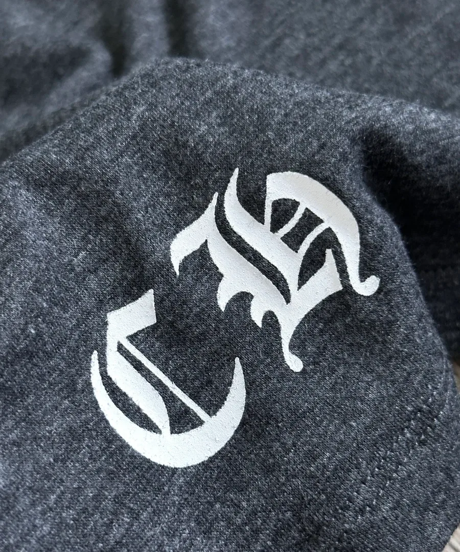 Деталь готического логотипа CH на подоле серой футболки Chrome Hearts