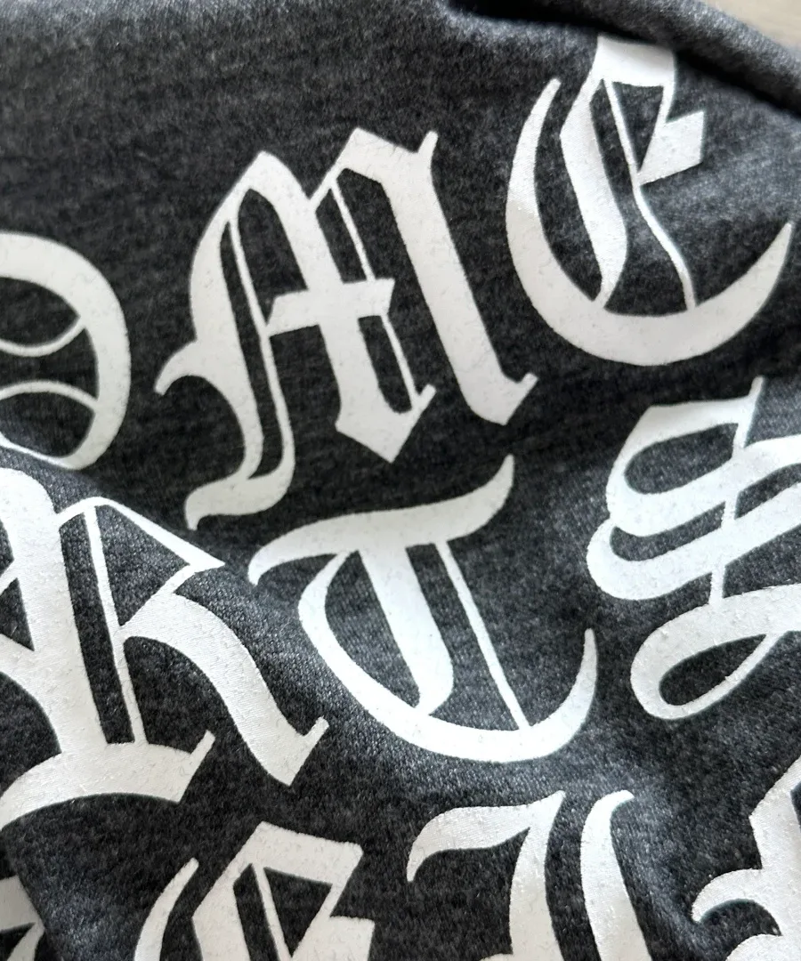 Крупный план готического текстового принта на спине серой футболки Chrome Hearts