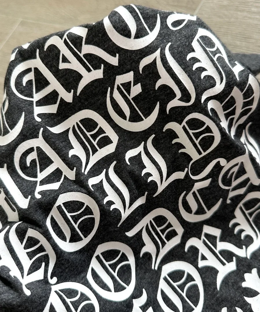 Деталь белого готического принта на серой меланжевой ткани футболки Chrome Hearts