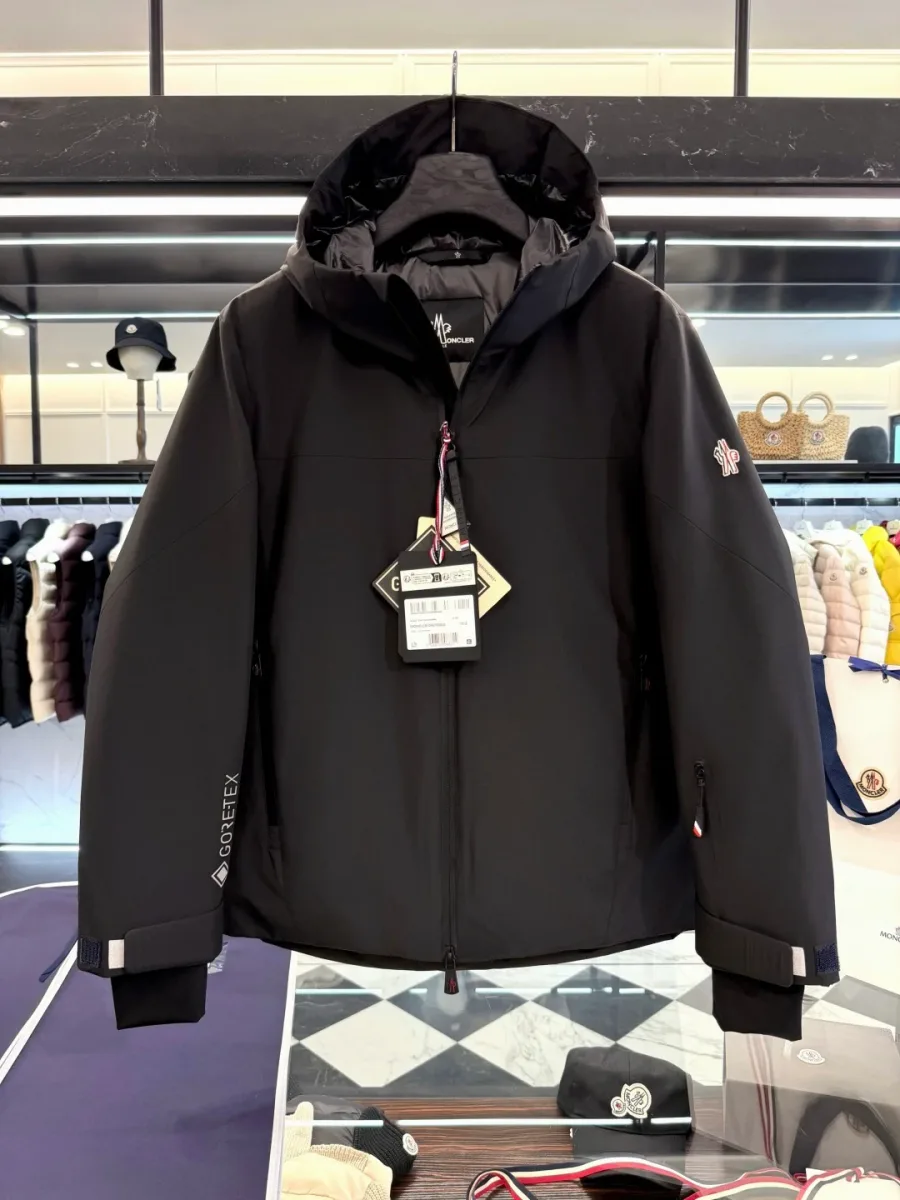 Чёрная пуховая куртка Moncler Grenoble с объёмным капюшоном и патчем на рукаве, фронтальный план на вешалке