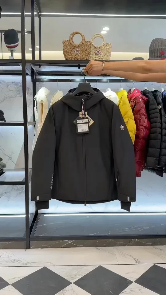 Чёрный пуховик Moncler Grenoble прямого кроя с капюшоном на вешалке в торговом зале, вид спереди