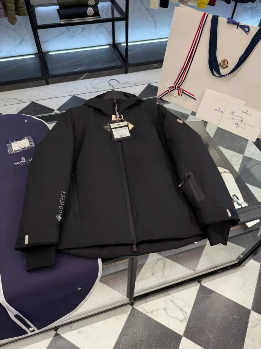 Чёрный пуховик Moncler Grenoble с маркировкой Gore-Tex на рукаве в разложенном виде рядом с упаковкой