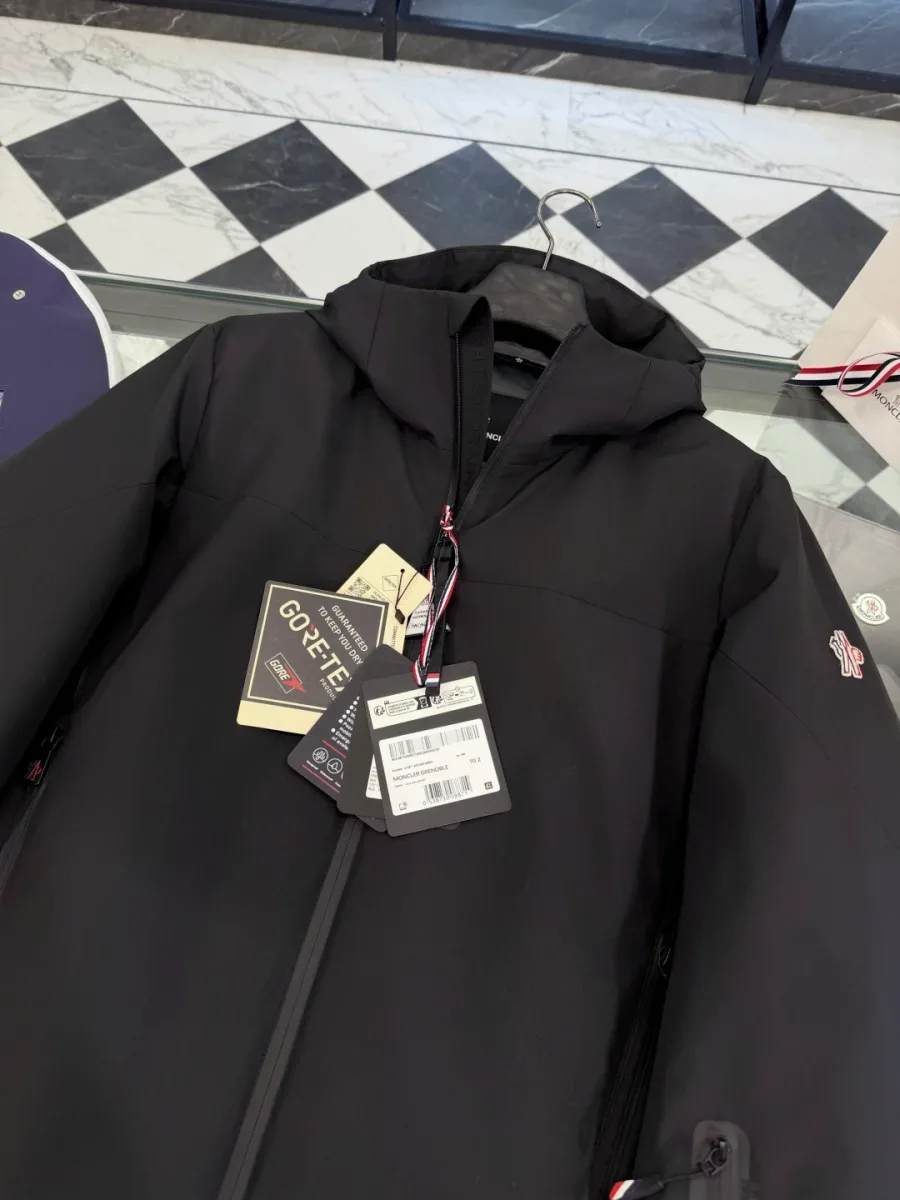 Детали горловины, капюшона и картонной бирки Gore-Tex на чёрном пуховике Moncler Grenoble крупным планом