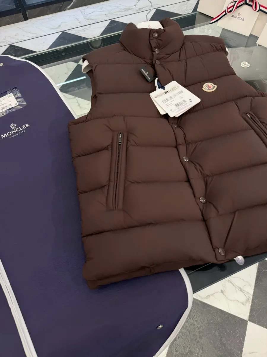 Коричневый пуховый жилет, вид спереди на стеклянном столе с чехлом Moncler