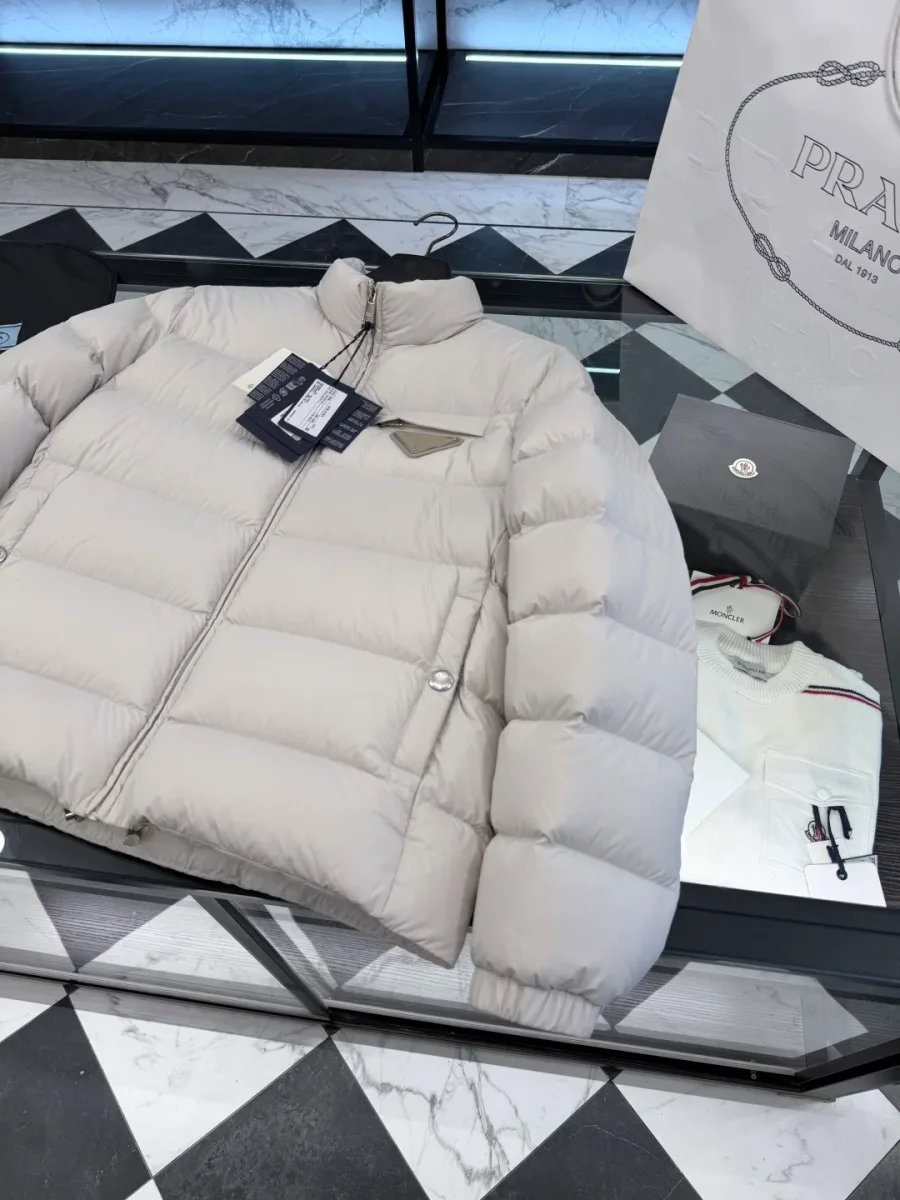 Левая сторона светло-бежевого пуховика Prada с боковым карманом на кнопке и треугольной эмблемой