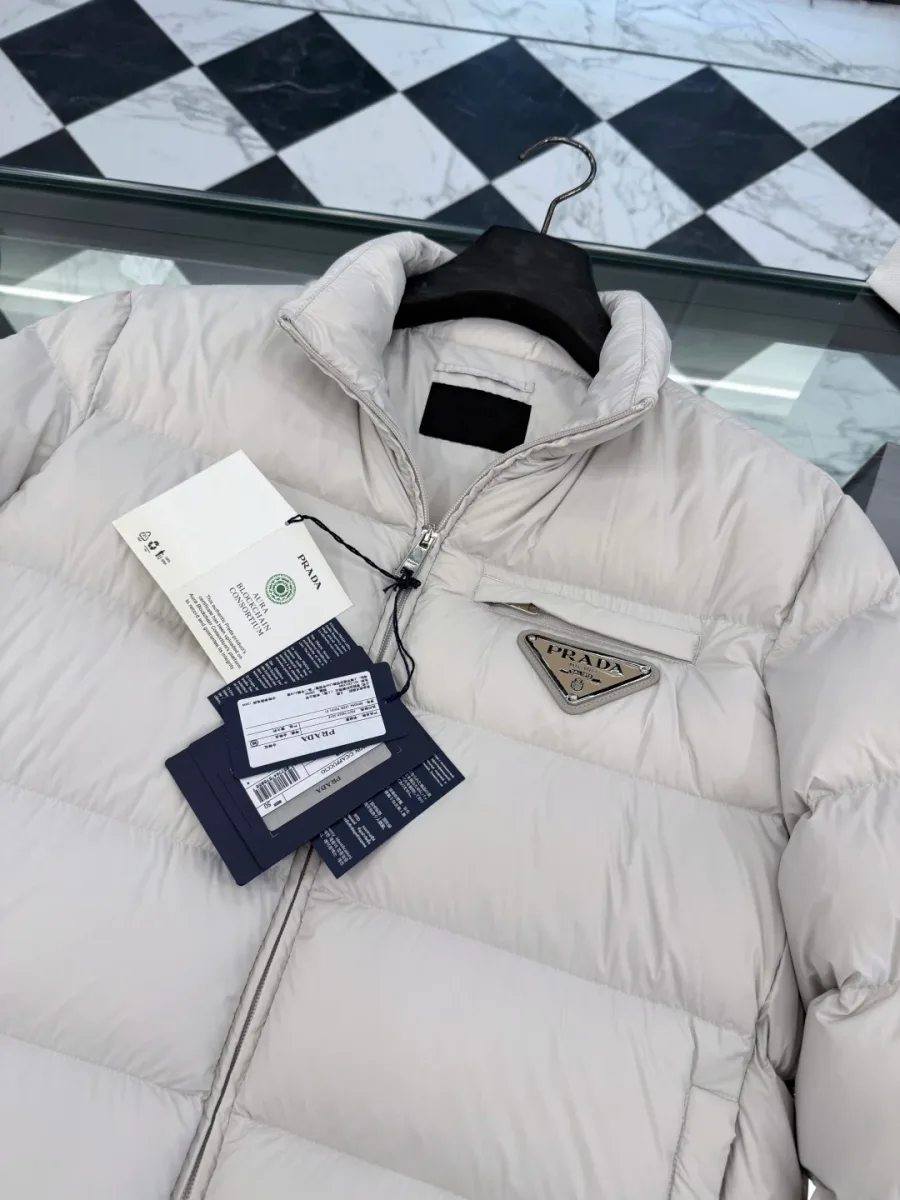 Крупный план горловины, комплекта бирок Re-Nylon и треугольного логотипа на груди пуховика Prada