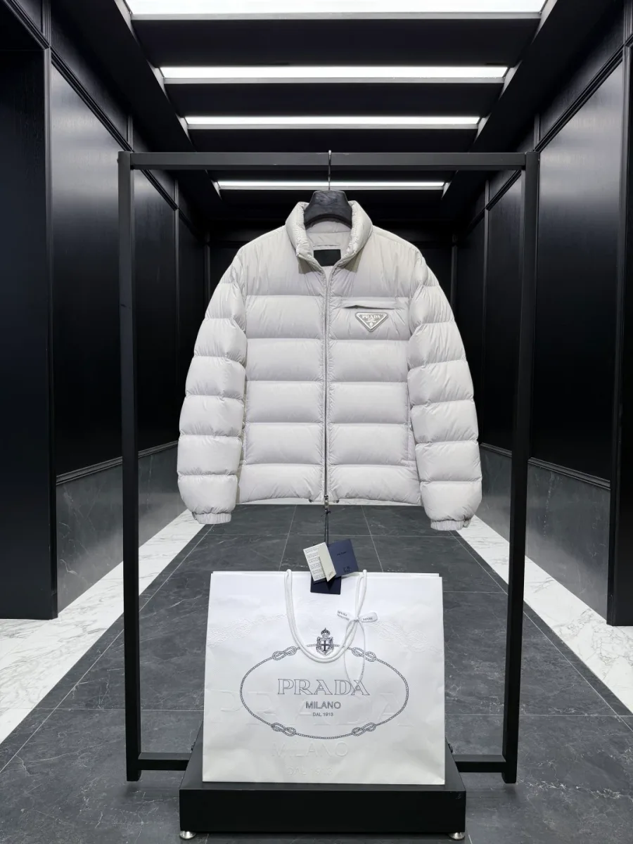 Застёгнутый светло-бежевый пуховик Prada с центральной молнией и треугольным логотипом спереди