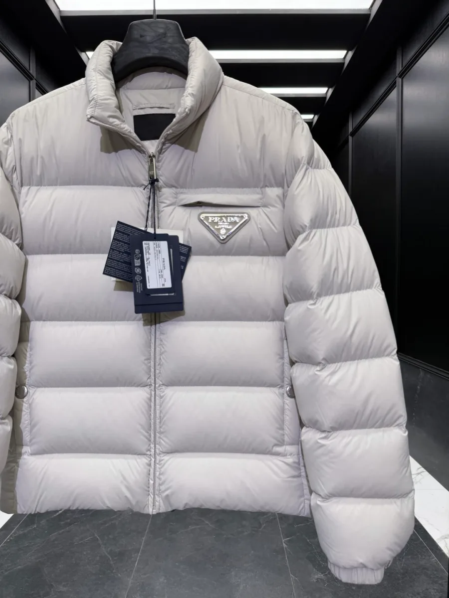 Верхняя часть светло-бежевого пуховика Prada с металлической молнией и шильдом на груди