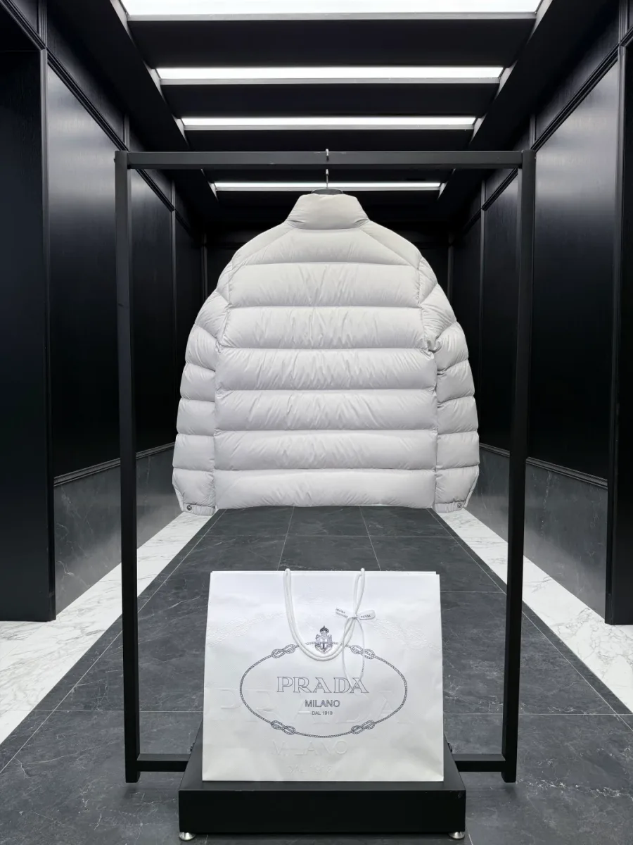 Вид сзади на светло-бежевый пуховик Prada с равномерной горизонтальной стёжкой на вешалке