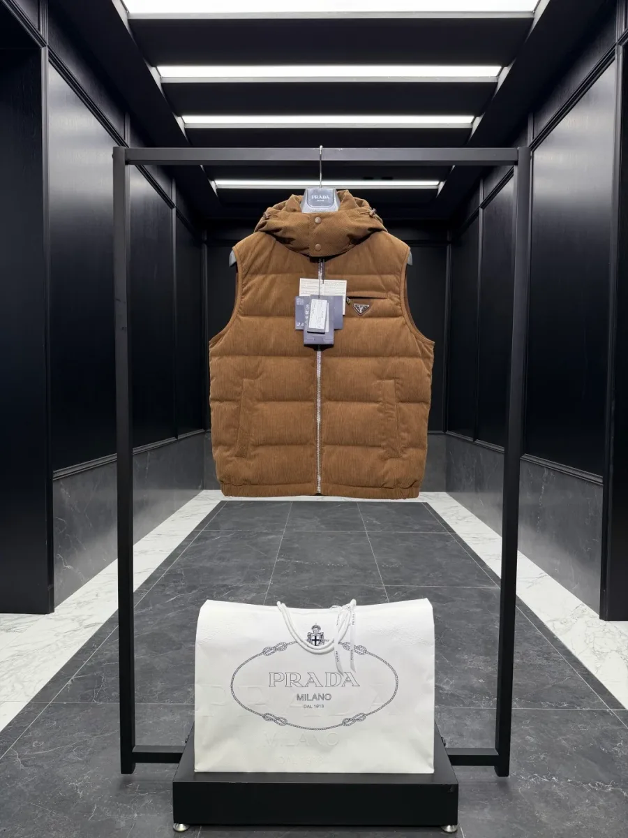 Коричневый стёганый вельветовый жилет Prada на стойке в интерьере бутика, вид спереди