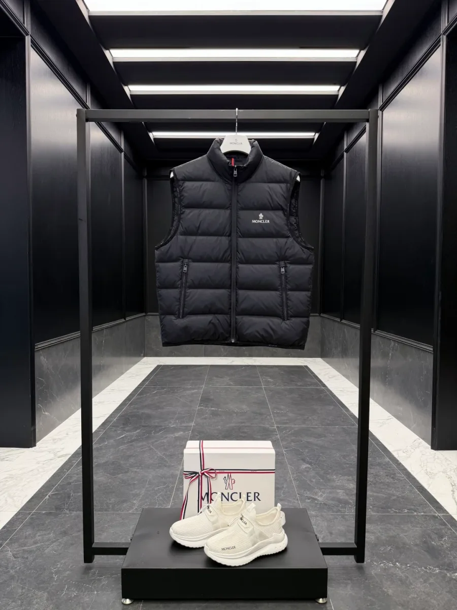 Чёрный стеганый жилет Moncler на стойке в интерьере, фронтальный ракурс