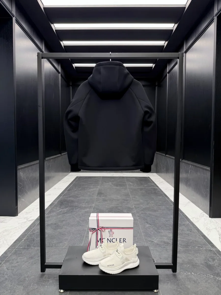 Чёрная куртка с капюшоном Moncler на стойке, вид со спины в интерьере