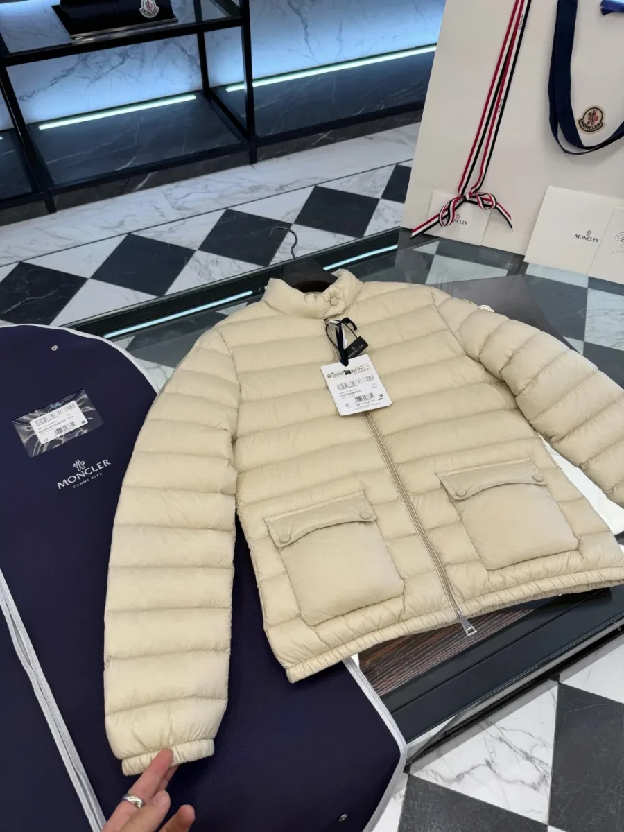 Бежевый пуховик Moncler Lans на стеклянном столе, вид сверху в три четверти