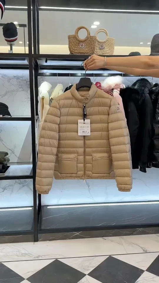 Бежевый пуховик Moncler Lans в руке на фоне интерьера