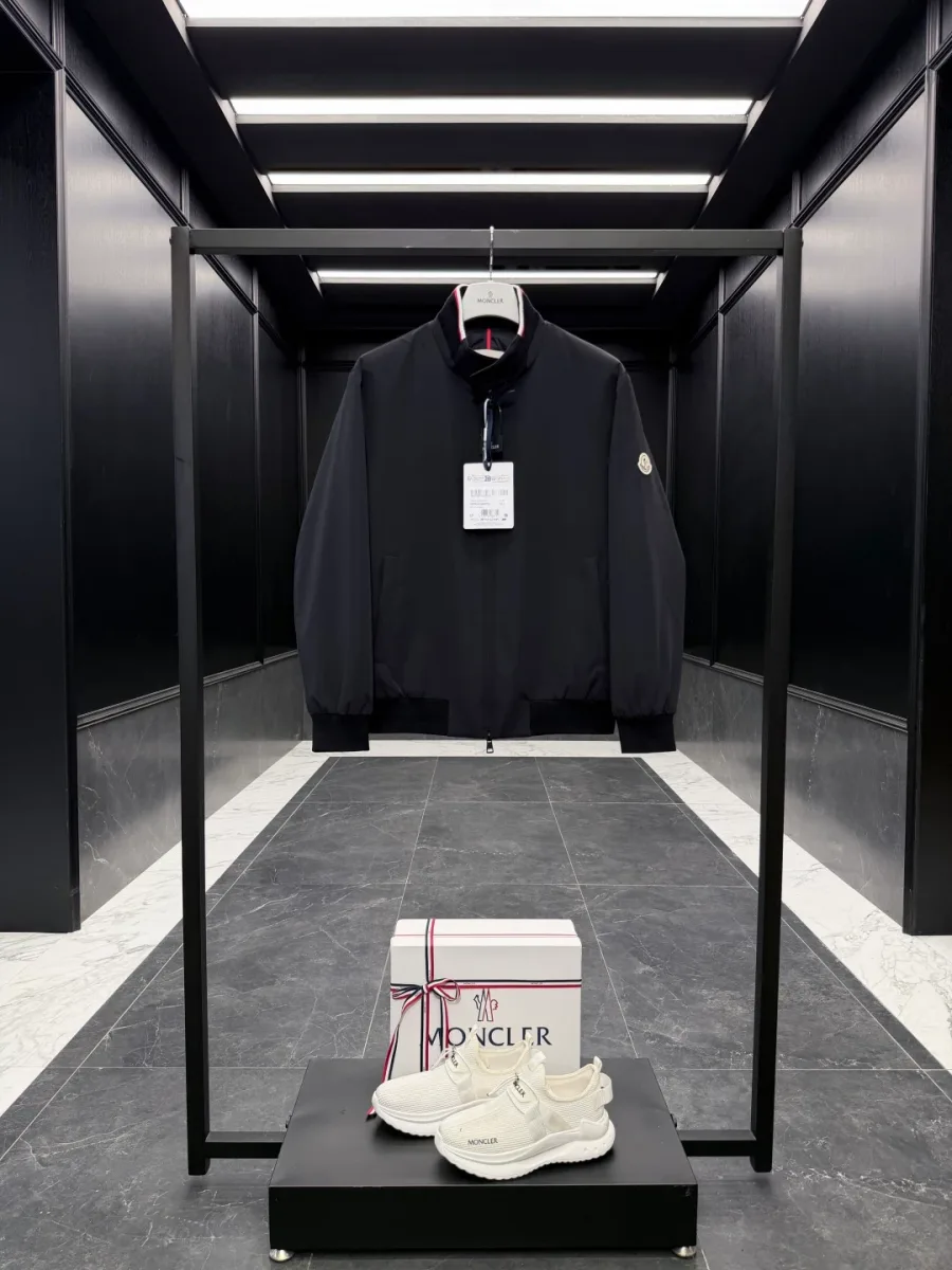 Чёрная куртка-бомбер Moncler Reppe на вешалке спереди с навесной биркой и патчем на рукаве