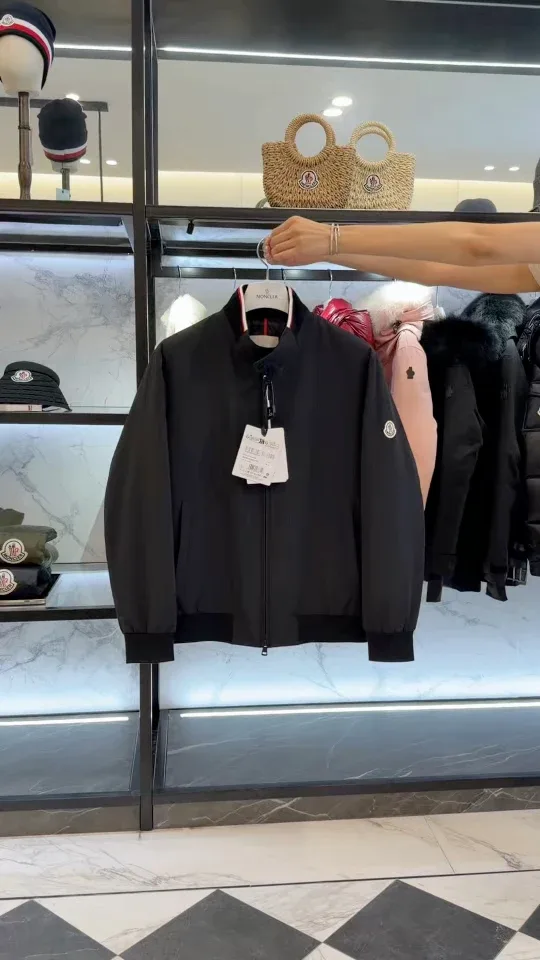 Общий план чёрной куртки-бомбера Moncler Reppe на вешалке в руке с видимым логотипом на рукаве