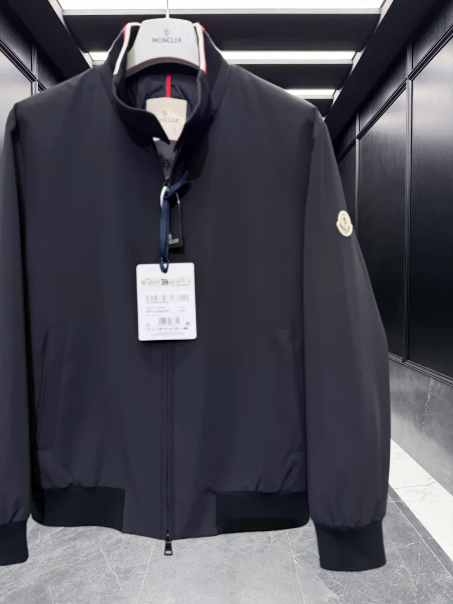 Средний план чёрной куртки Moncler Reppe с застёжкой-молнией и круглым шевроном на левом рукаве