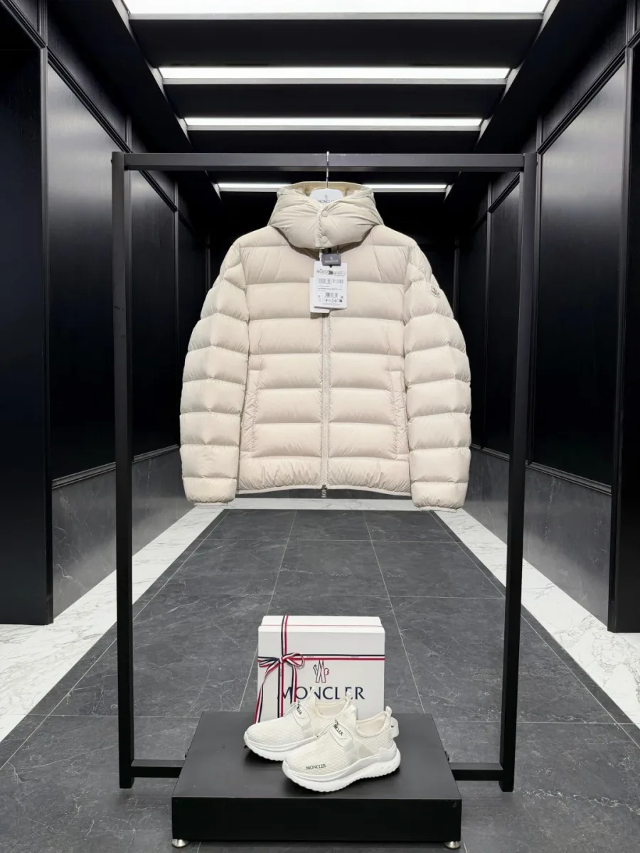 Бежевый стеганый пуховик Moncler с капюшоном на стойке-вешалке в витрине