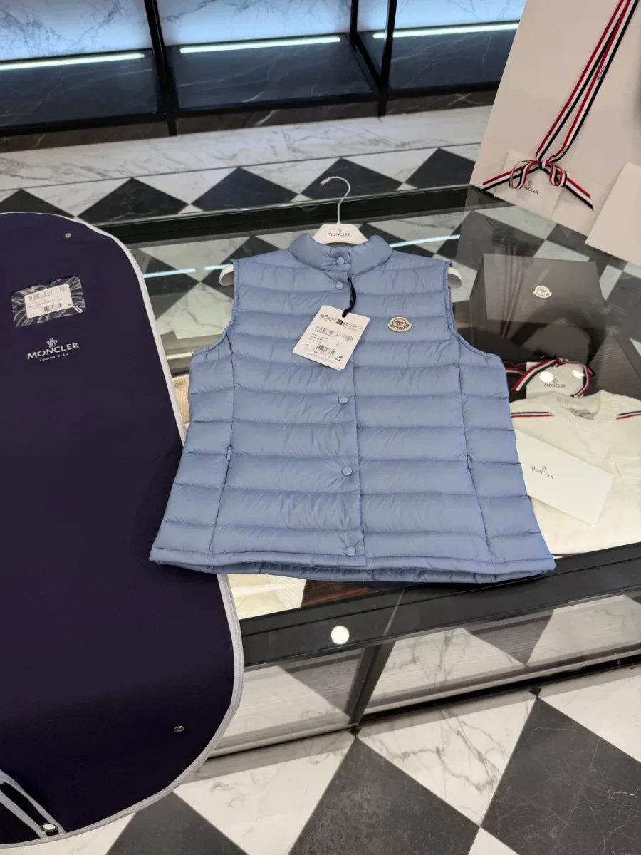 Светло-голубой пуховый жилет Moncler рядом с фирменным синим чехлом