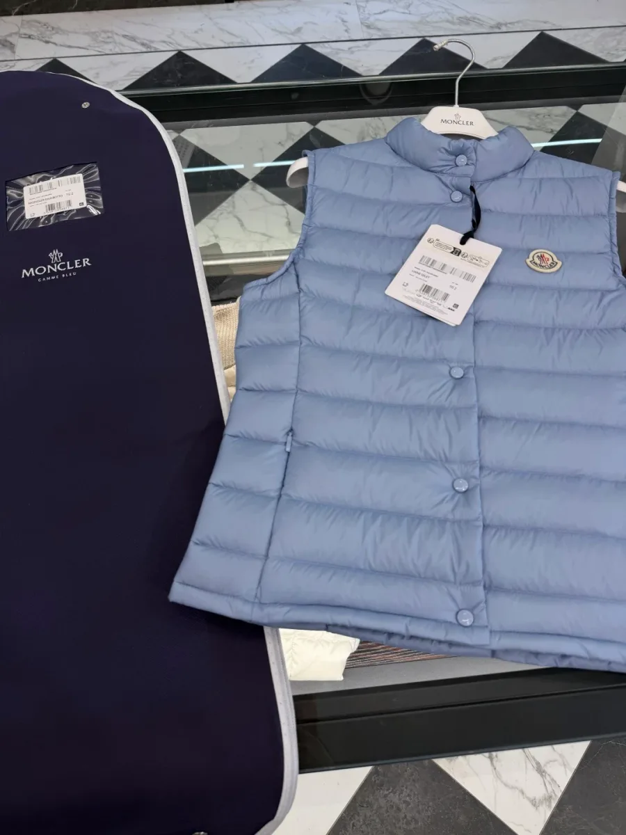 Жилет Moncler Liane светло-голубого цвета на вешалке рядом с чехлом для одежды