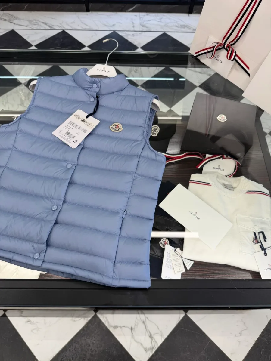 Светло-голубой пуховый жилет Moncler крупным планом на стеклянном столе