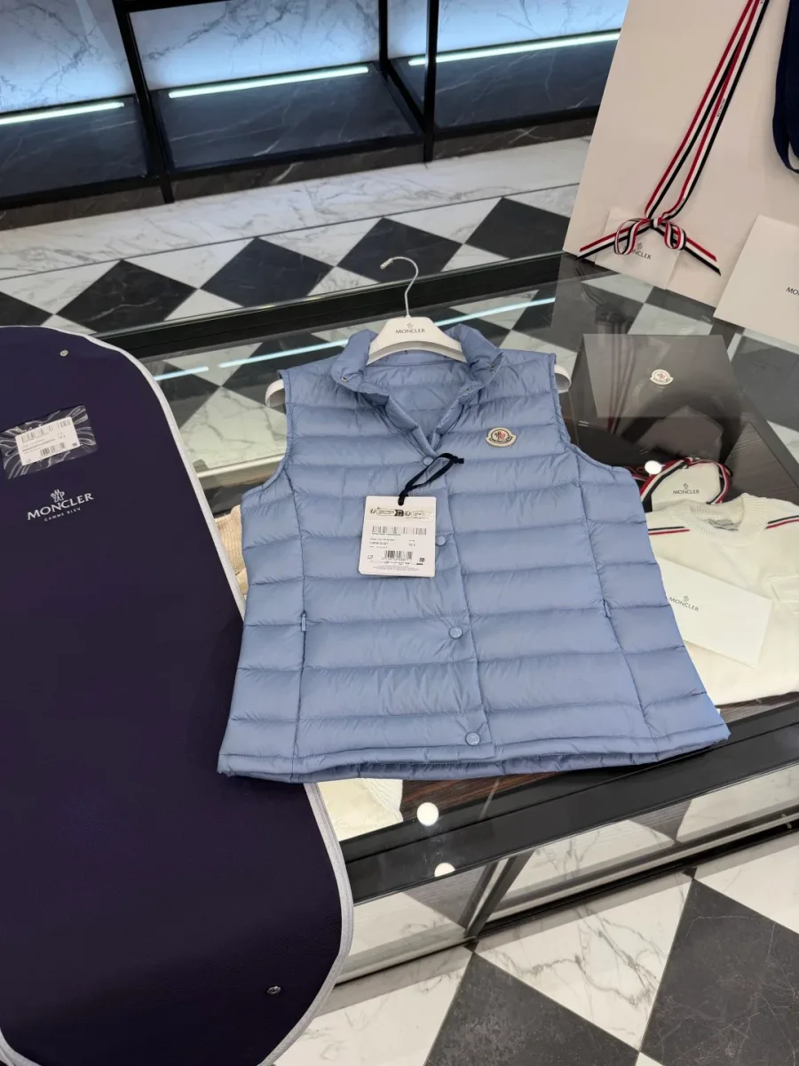 Светло-голубой жилет Moncler Liane с бирками на столе рядом с чехлом