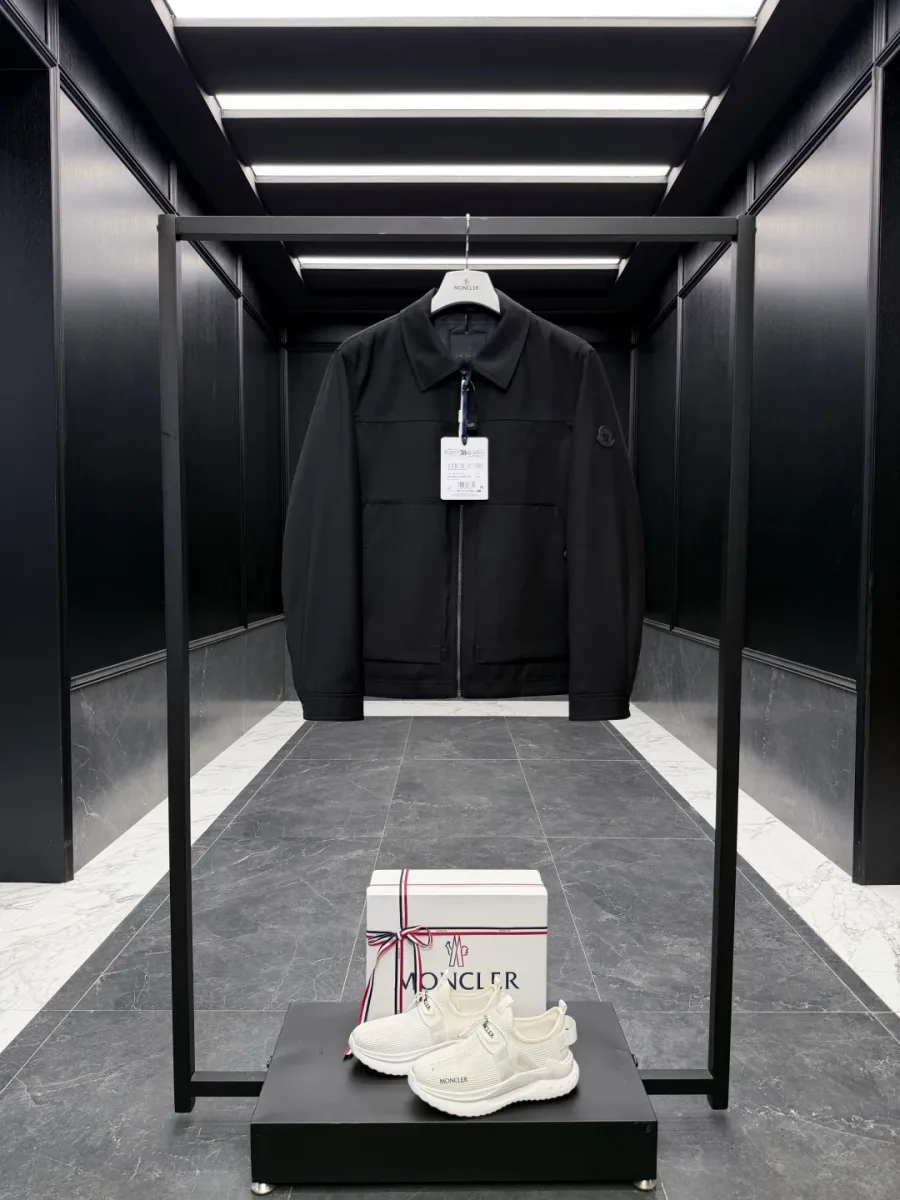 Чёрная куртка Moncler на вешалке в интерьере шоурума, вид спереди в полный рост.