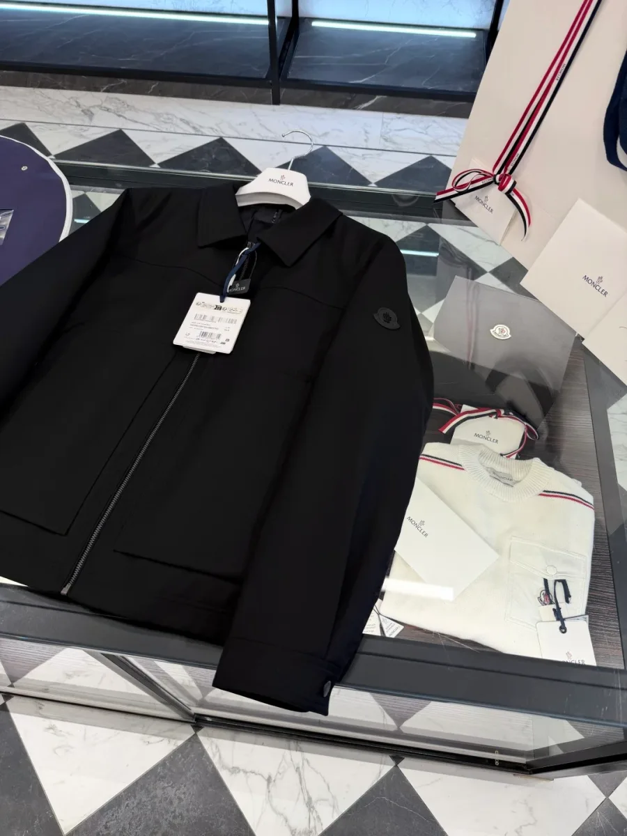 Чёрная куртка Moncler под углом с навесными бирками и чехлом на фоне.