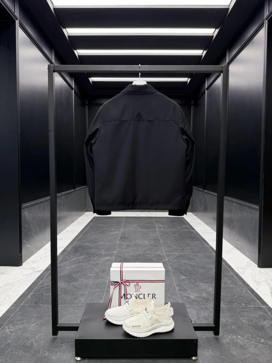 Чёрная куртка Moncler на стойке, вид со спины на общем плане интерьера.