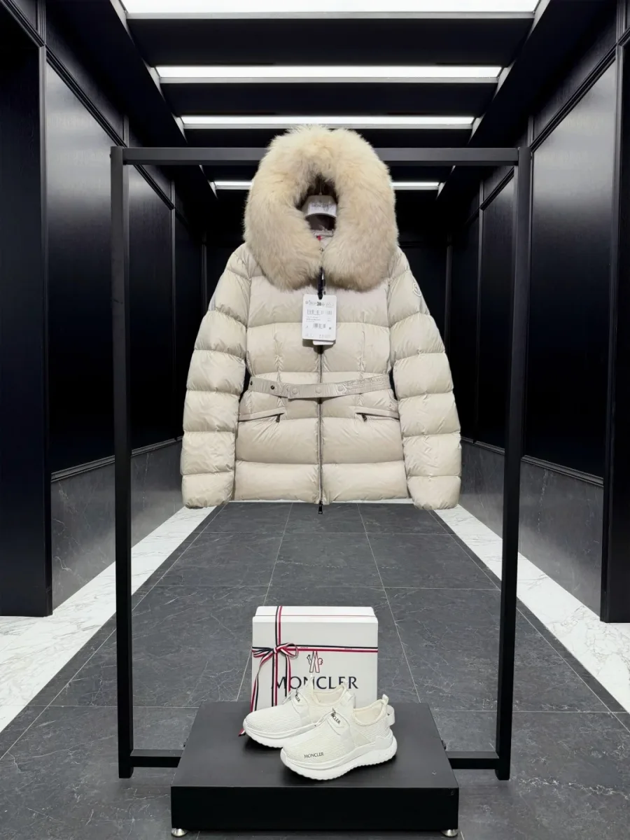 Бежевый пуховик Moncler с меховым капюшоном и поясом, вид спереди в интерьере