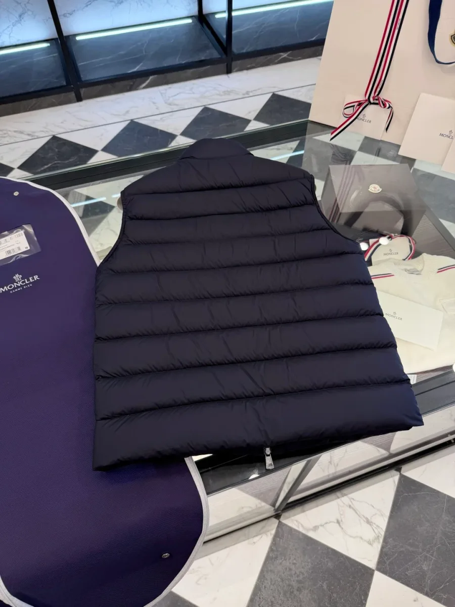 Вид со спины на тёмно-синий жилет Moncler с горизонтальной стёжкой на стеклянной поверхности