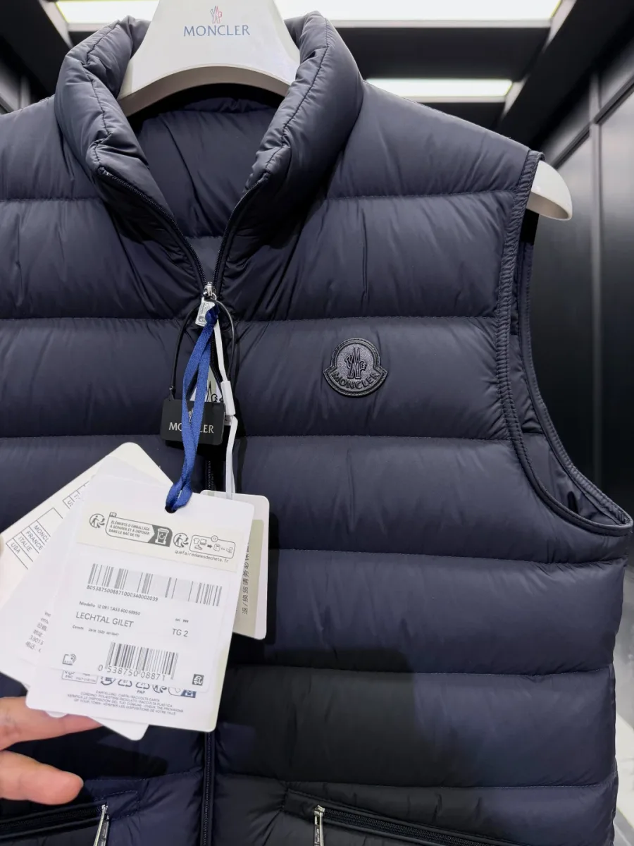 Крупный план верхней части тёмно-синего жилета Moncler с монохромным патчем на груди и бирками