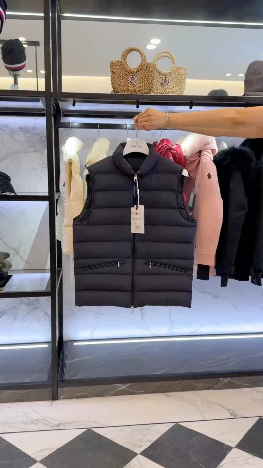 Тёмно-синий стёганый жилет Moncler на плечиках на фоне витрины шоурума, вертикальный ракурс