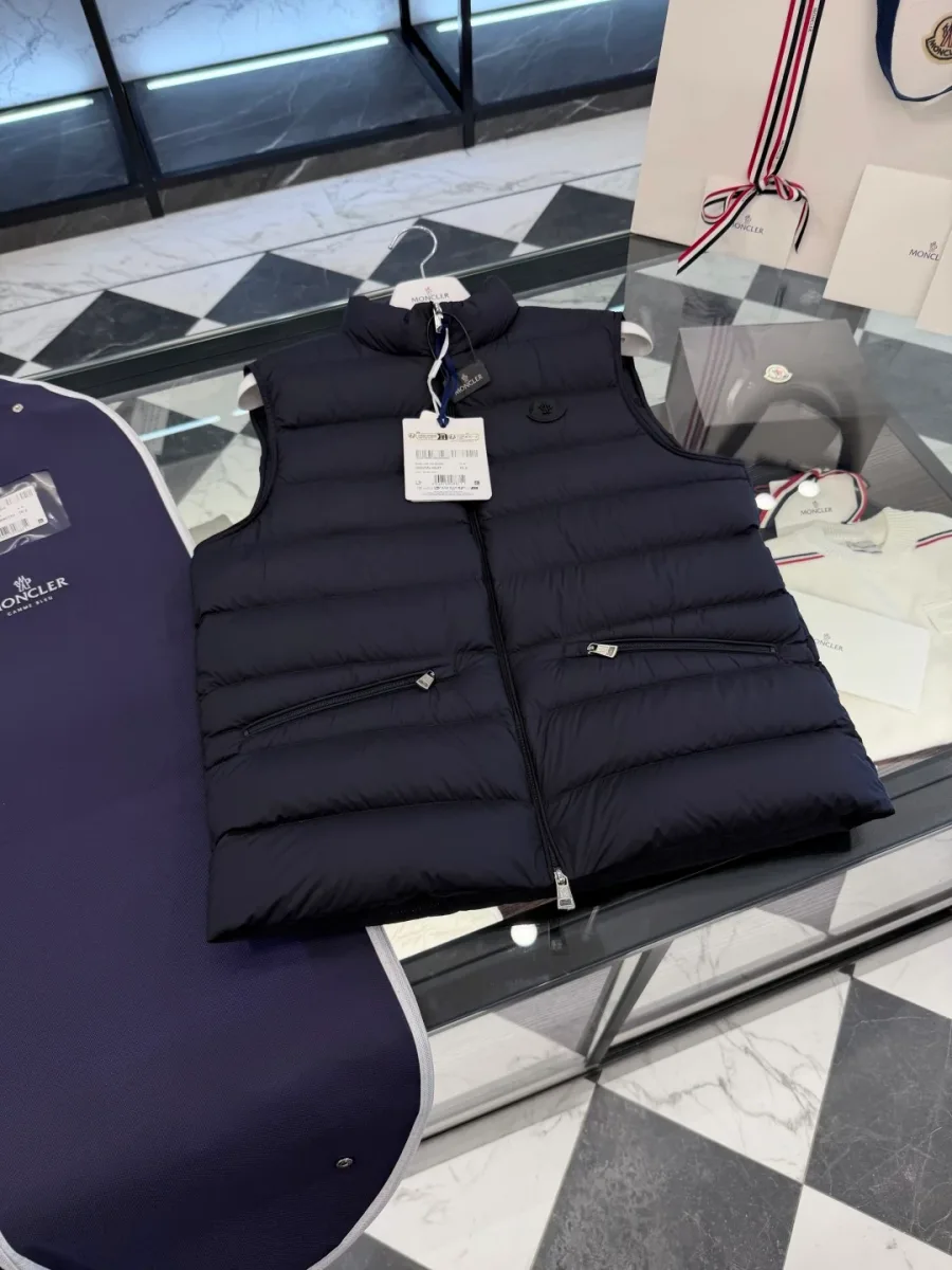 Тёмно-синий жилет Moncler в разложенном виде на стеклянной витрине, диагональный ракурс сверху