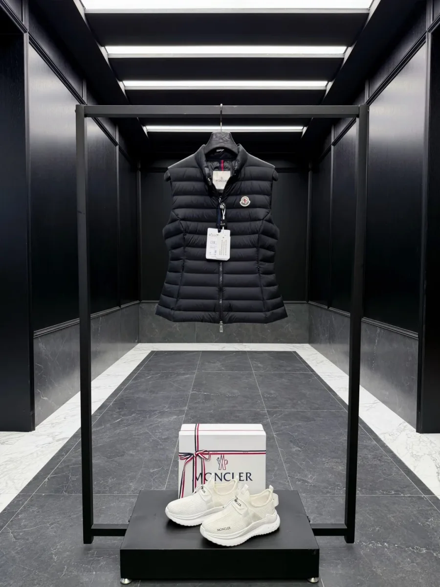 Чёрный пуховый жилет Moncler на вешалке, фронтальный ракурс на стойке