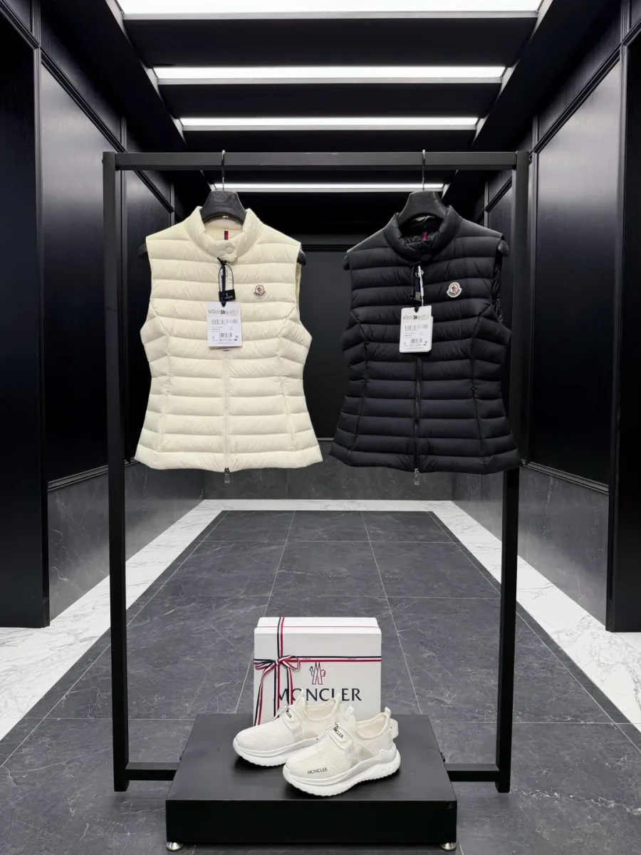 Чёрный и белый пуховые жилеты Moncler на вешалке, фронтальный план