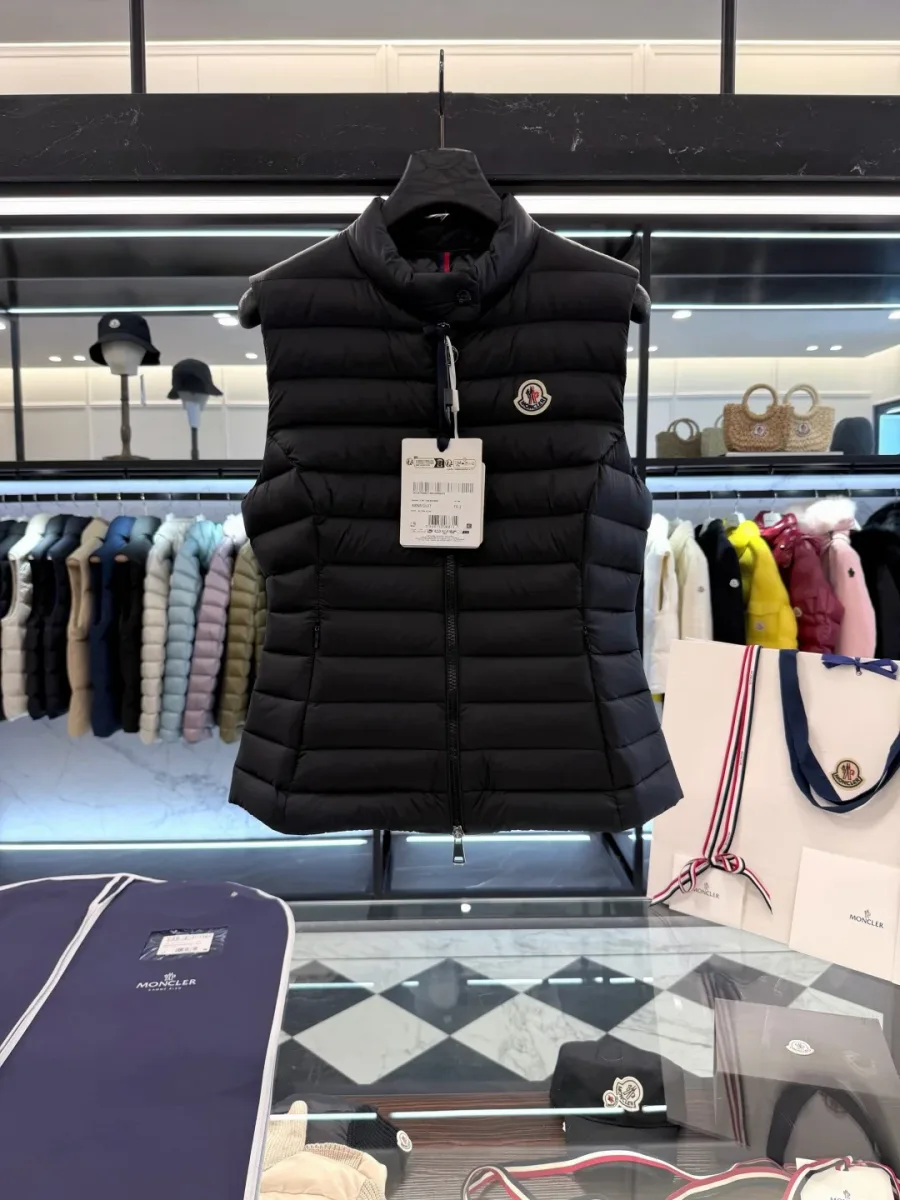 Чёрный пуховый жилет Moncler на вешалке на фоне фирменного синего чехла