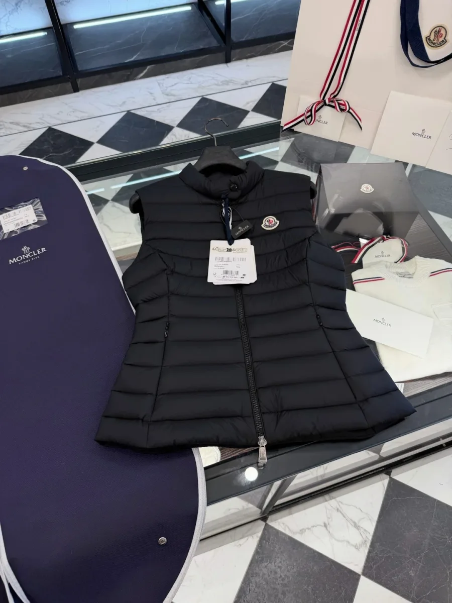 Чёрный стеганый жилет Moncler на столе рядом с фирменным синим кофром