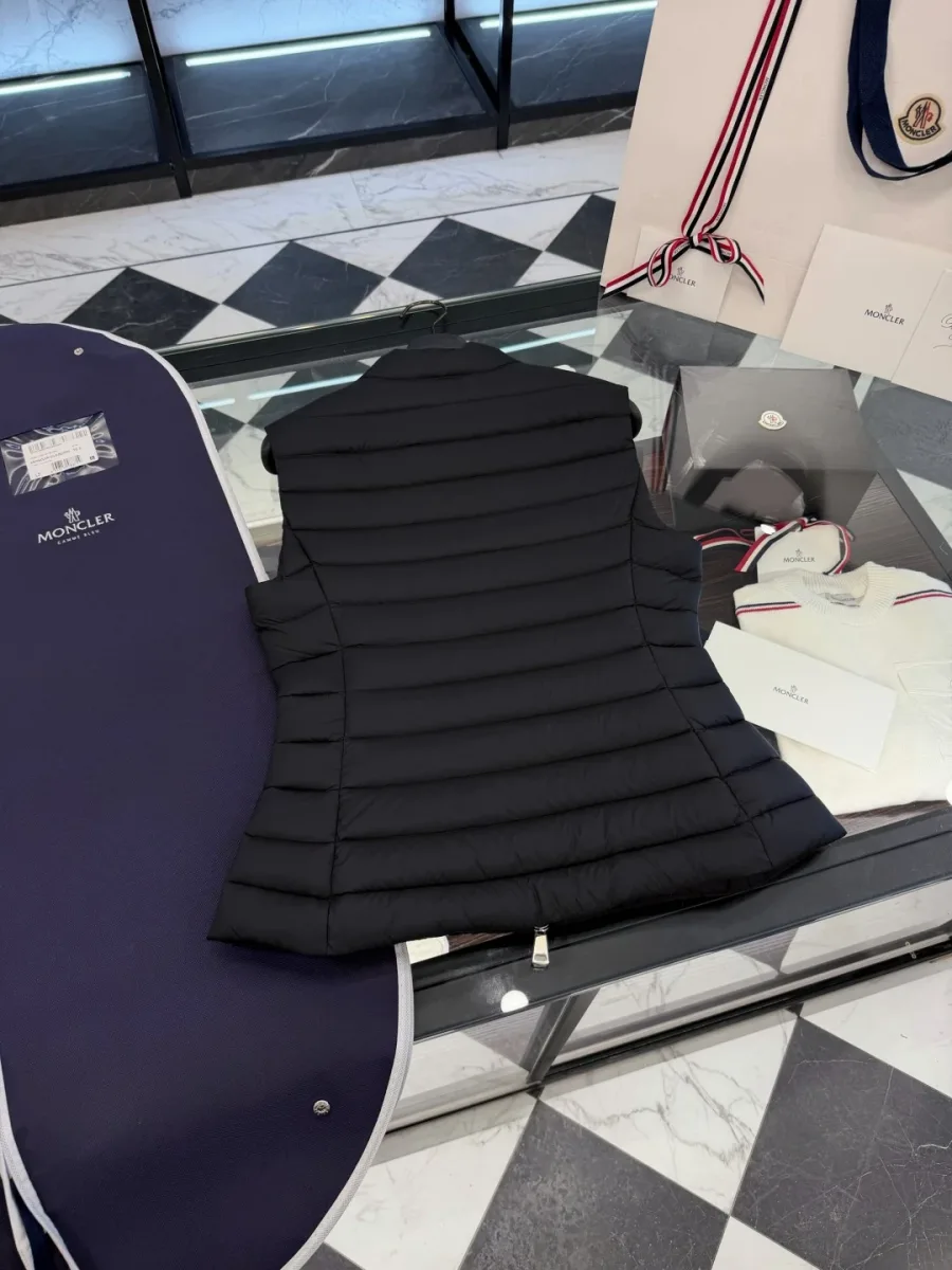 Вид сзади чёрного стеганого жилета Moncler на столе рядом с чехлом