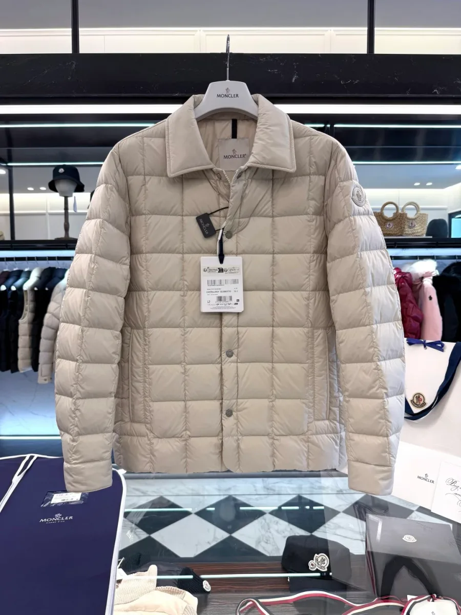 Пуховик-рубашка Moncler бежевого цвета на вешалке над витриной магазина
