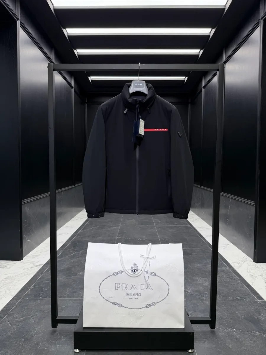 Чёрная куртка Prada Linea Rossa на рейле, вид спереди, красная полоса логотипа на груди и воротник-стойка