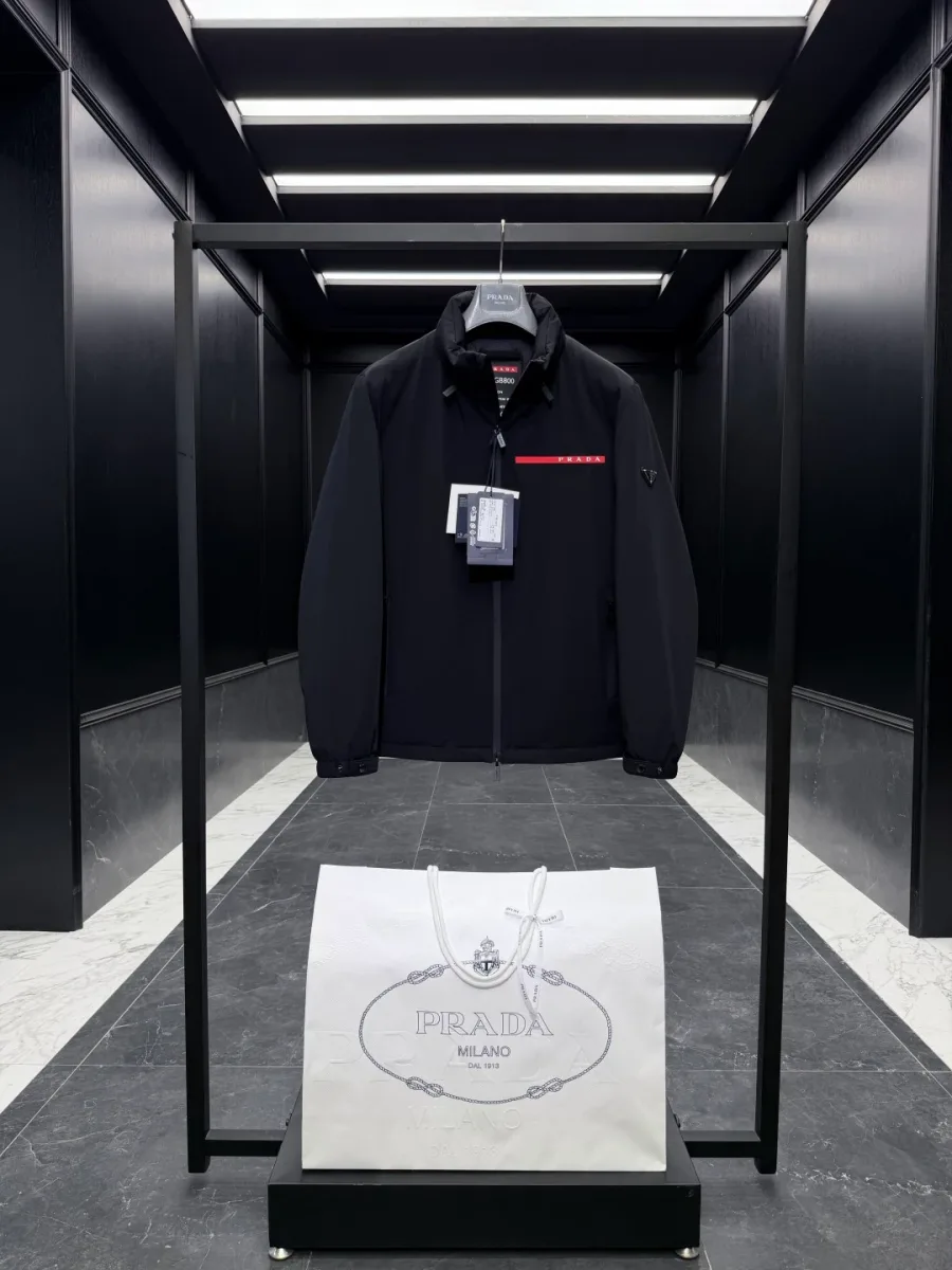 Чёрная утеплённая куртка Prada на вешалке, фронтальный ракурс, прямая посадка и застёжка на молнию
