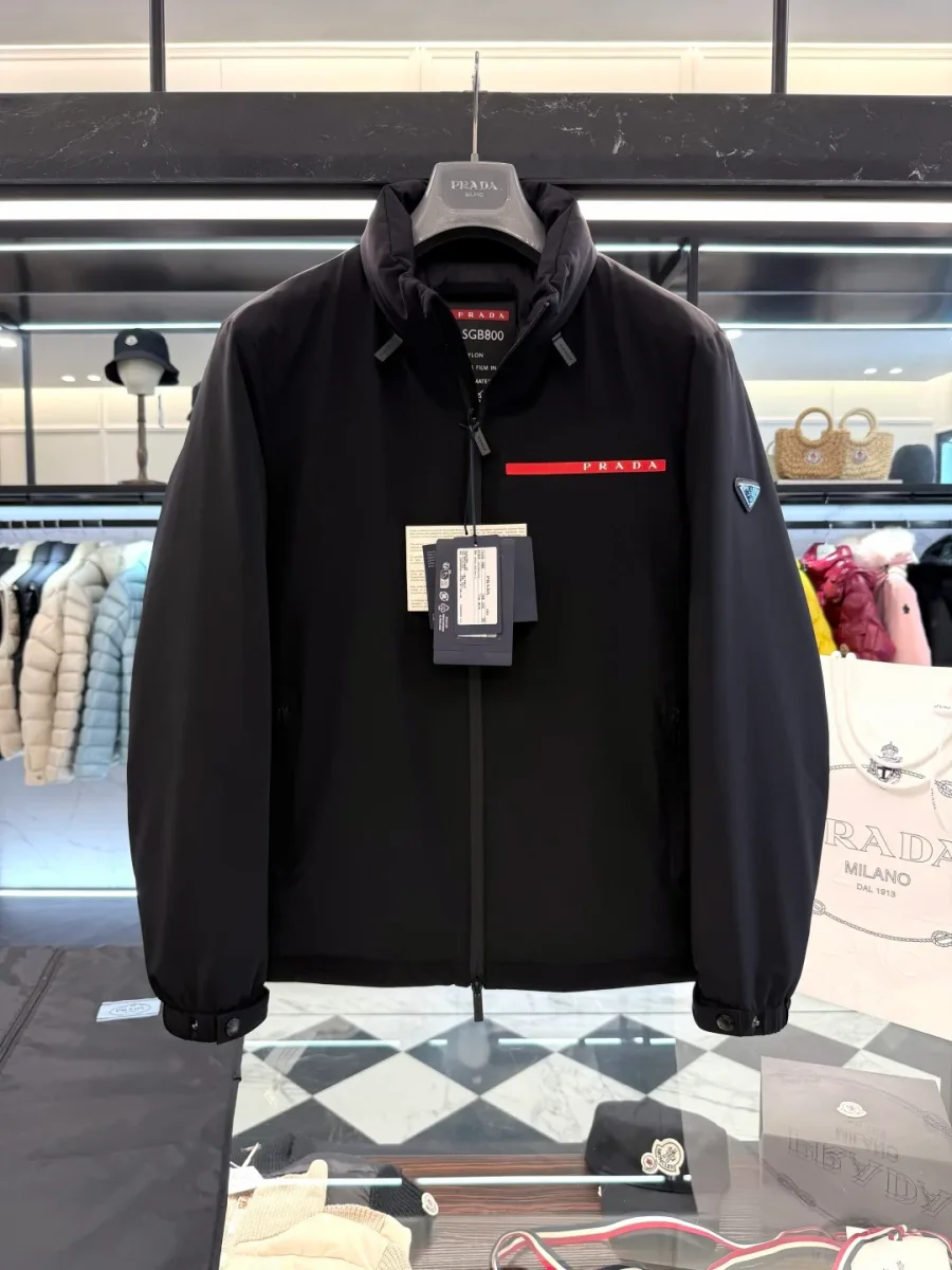 Фронтальный ракурс чёрной куртки Prada Linea Rossa с высоким воротником и металлическим шильдиком