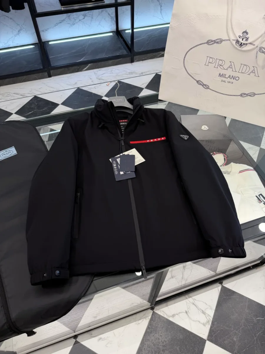 Чёрная куртка Prada Linea Rossa на стеклянной поверхности, общий вид спереди с навесными бирками
