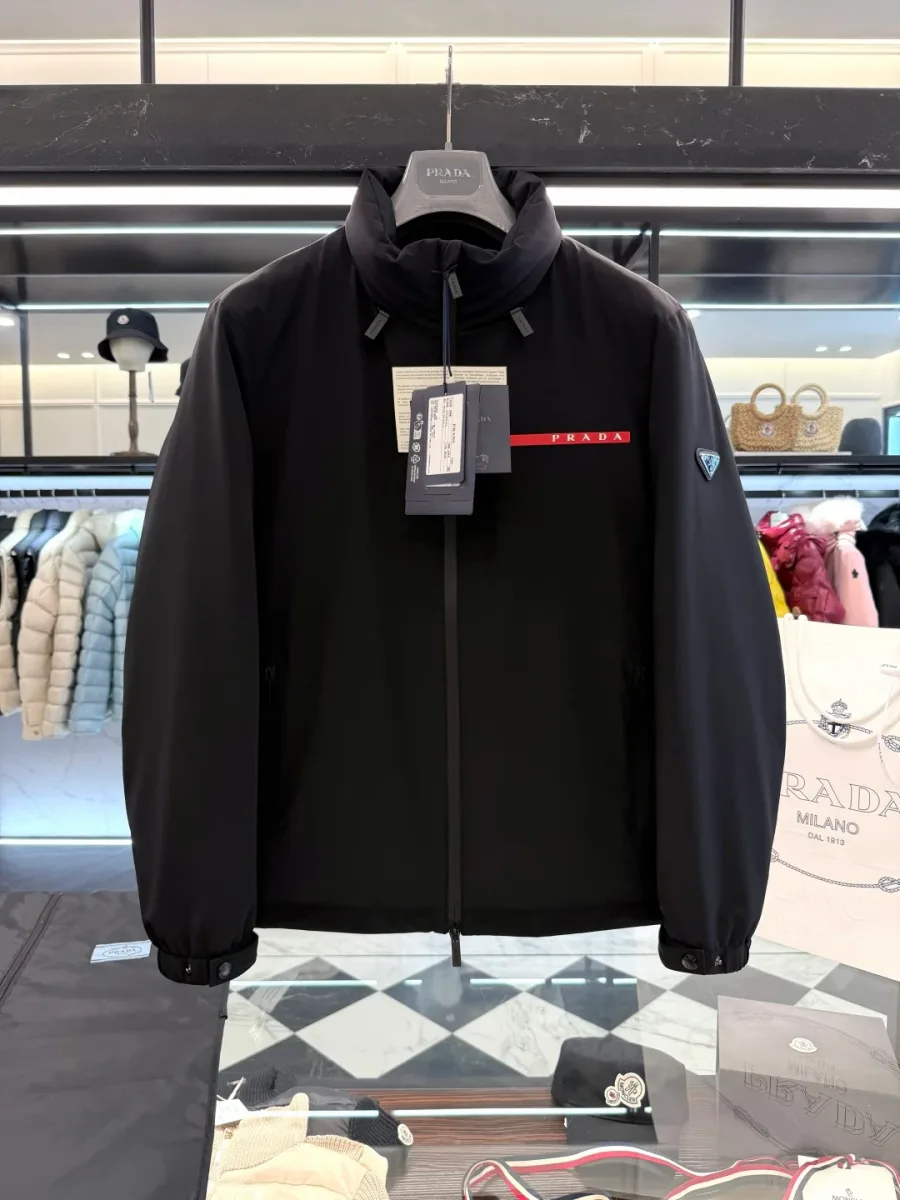 Чёрная куртка Prada на вешалке в интерьере, вид спереди, матовый нейлон и контрастная красная вставка