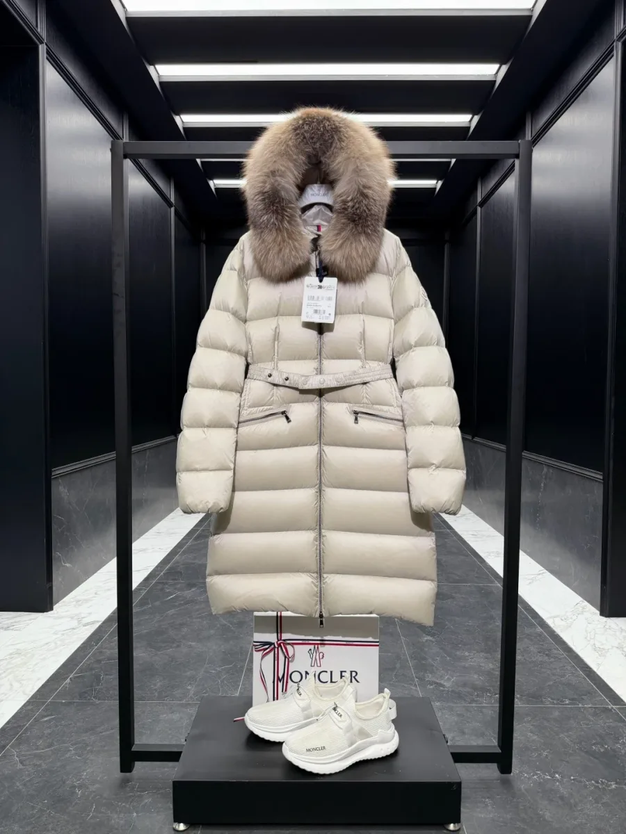 Бежевый удлинённый пуховик Moncler с меховым капюшоном и поясом, вид спереди на стойке