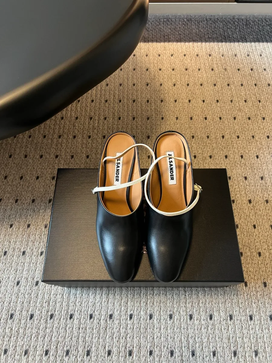 Чёрные кожаные мюли Jil Sander с круглым мысом и белым ремешком, вид спереди на фирменной коробке